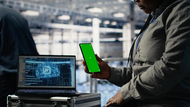 Technician using green screen smartphone in server hub while optimizing deep learning systems handling tasks. Data center worker uses chroma key phone, adjusting AI model parameters photo