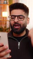 indisk man på Hem öppnas ögon bred och hissar ögonbryn medan ser på smartphone med chockade Lycklig reaktion. arab kille på soffa gester Wow med hand, överraskad förbi oväntat Bra meddelande. video