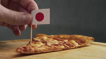 makro se av tunn pizza skiva med japansk flagga på pinne, scen länkar maträtt till japansk stil pålägg, lokal- mjuk ost och mjöl från regional kvarnar. video