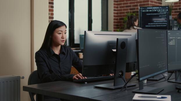 Asian programmer develops software at a computer desk, connecting source code, database work and digital workflow, inside a database development setup. video