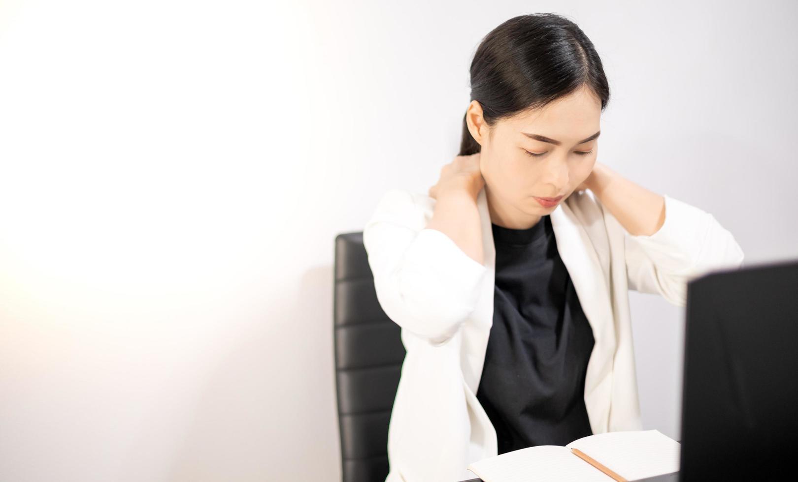giovani asiatici che si sentono dolorosi dal lavoro, seduti davanti al laptop nella loro casa. sindrome dell'ufficio della donna che lavora di concetto. foto