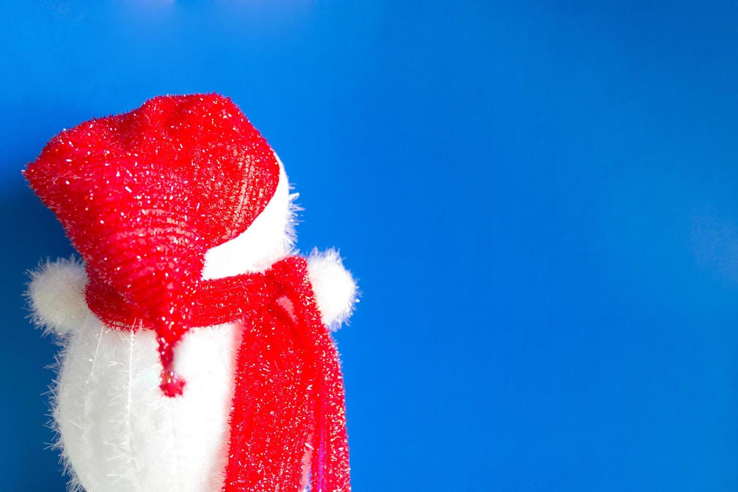 sfondo di natale della bambola del pupazzo di neve con un cappello rosso e una sciarpa rossa in piedi all'indietro. foto