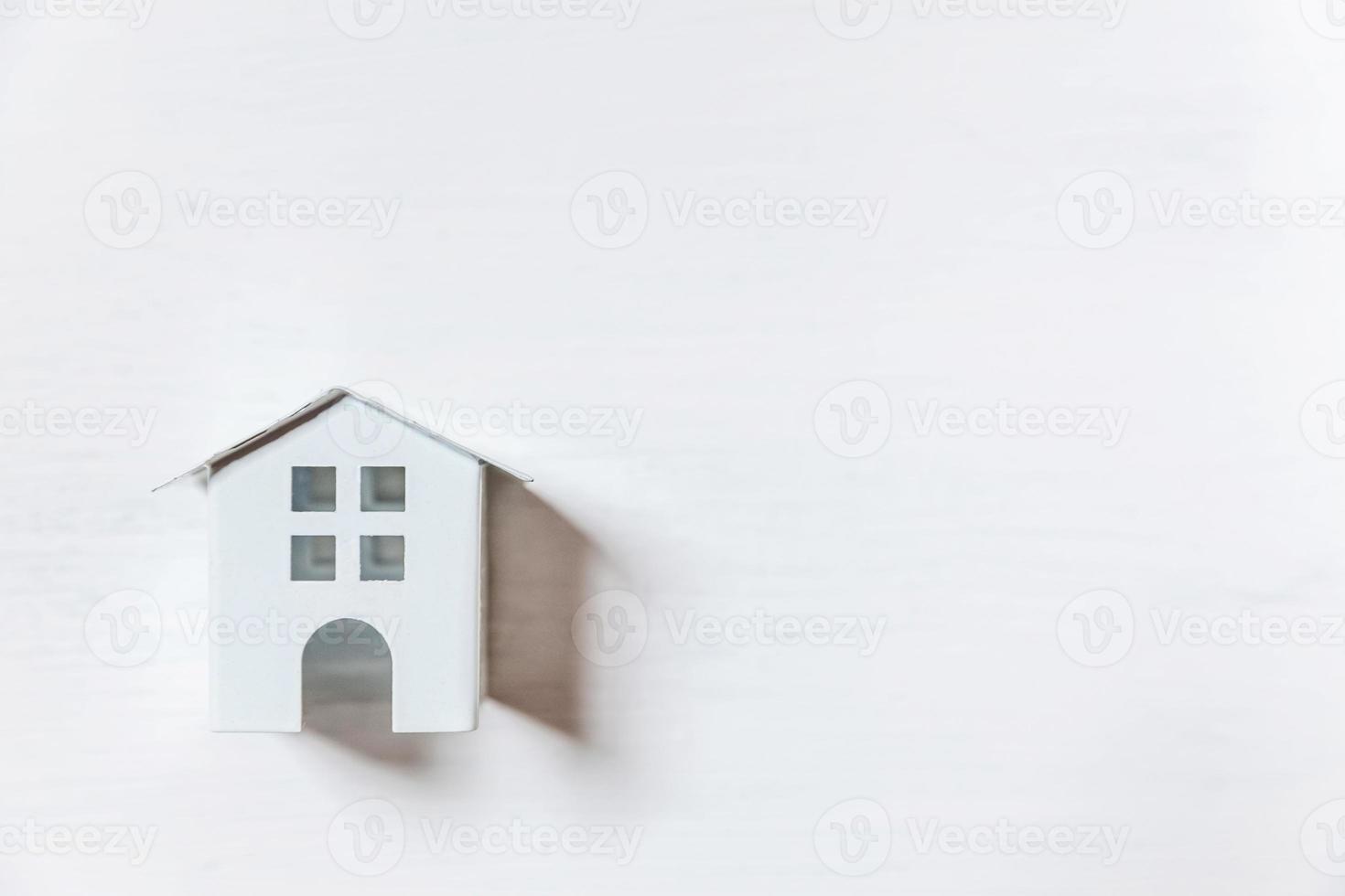 design semplicemente minimale con casa giocattolo in miniatura isolata su sfondo bianco. concetto di casa da sogno di assicurazione sulla proprietà ipotecaria. vista dall'alto piatta, copia spazio foto