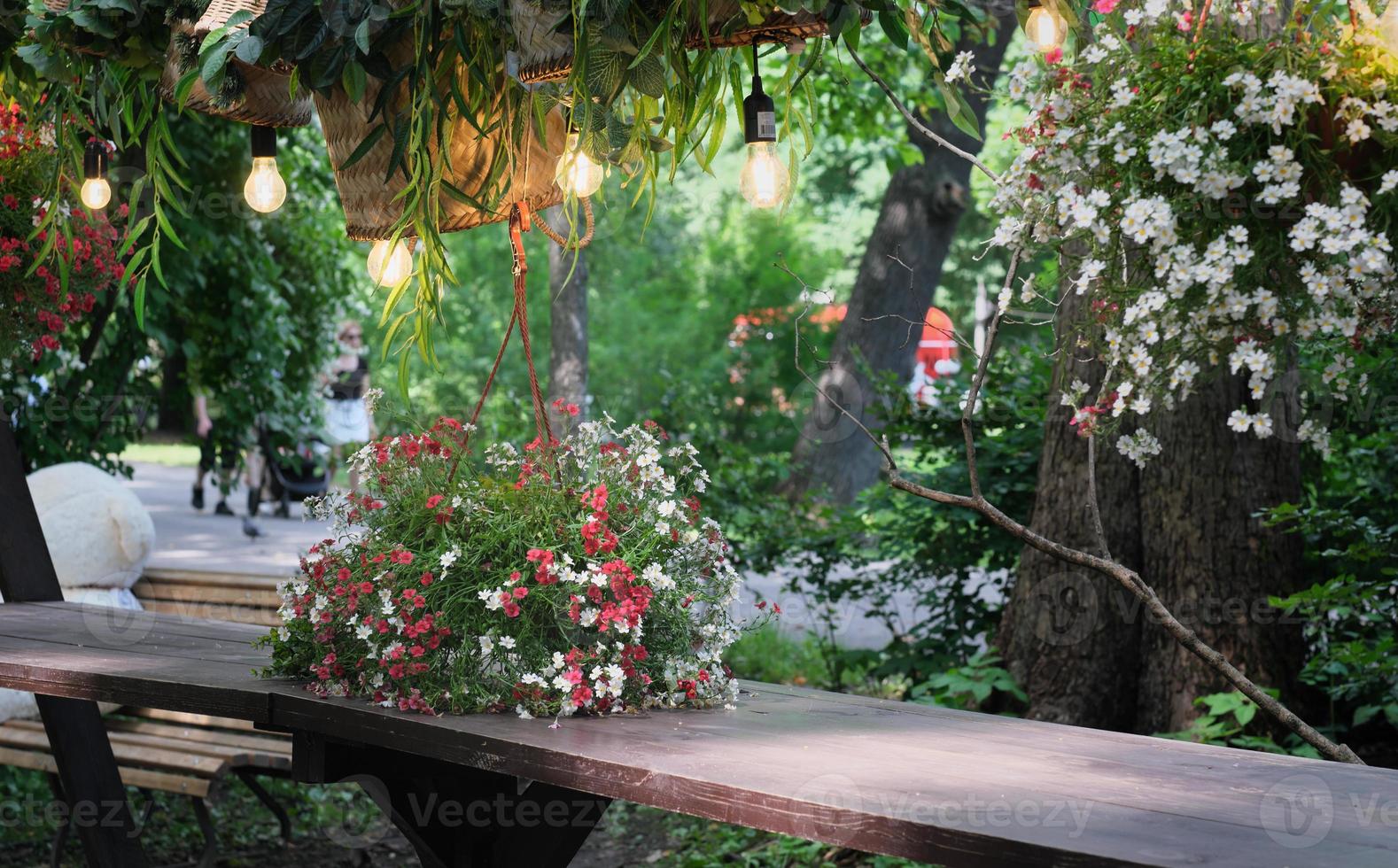 bellissimo posto romantico al caffè di strada in un parco. tavolo in legno decorato con fiori e cesti di vimini. lampade appese sopra un tavolo. posto per riposarsi e uscire insieme. foto