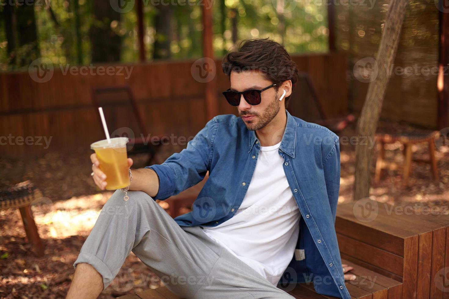 giovane uomo bello serio in abbigliamento casual con pausa pranzo, con in mano un bicchiere di tè freddo foto