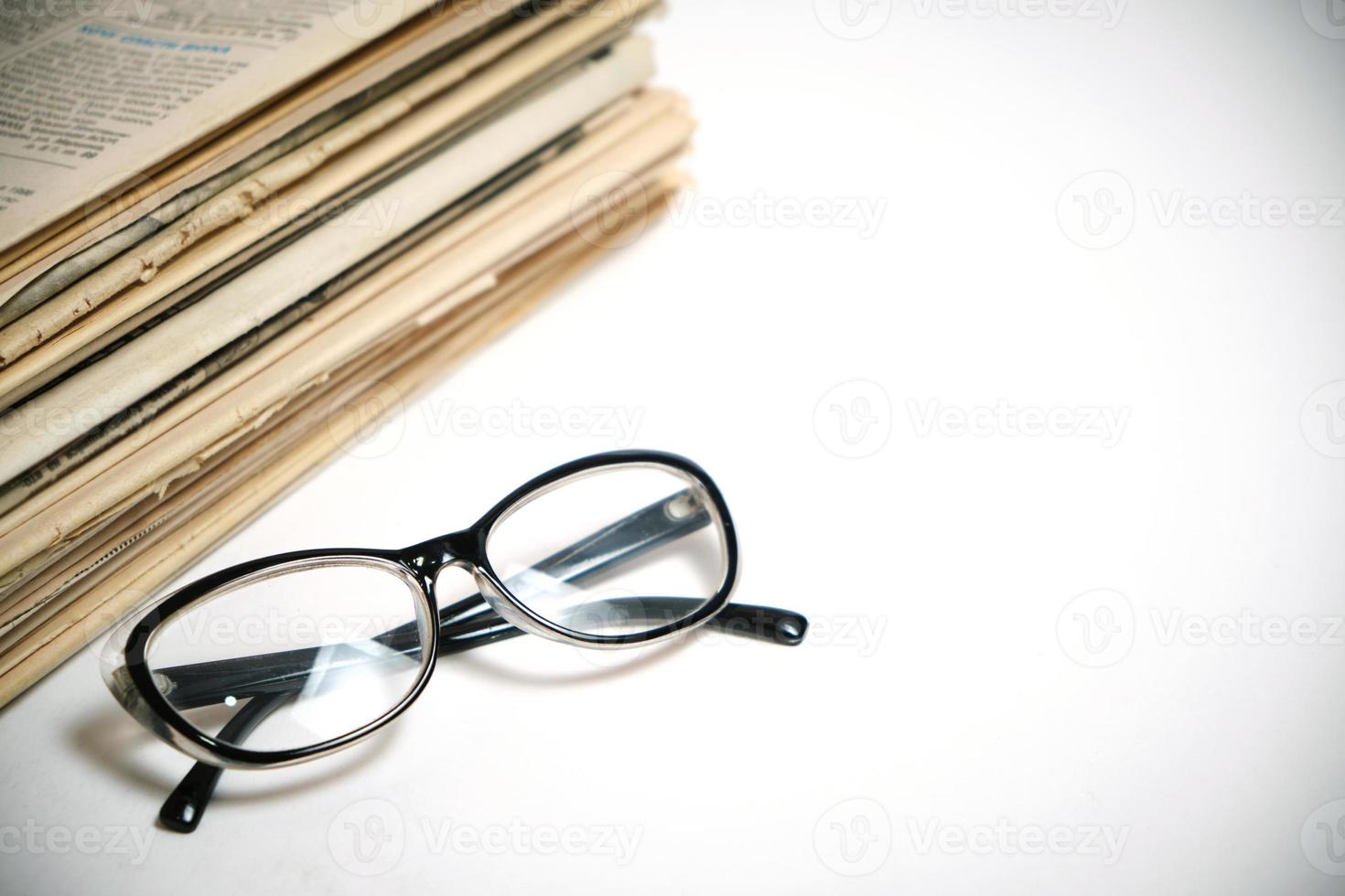 pila di vecchi giornali e occhiali da lettura su sfondo bianco. foto