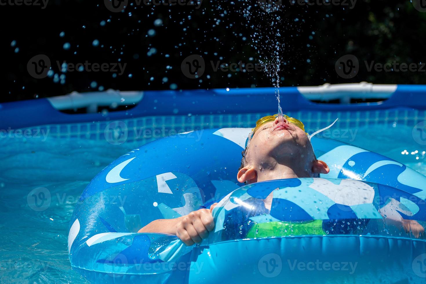 giovane ragazzo che sputava acqua verso l'alto nella piscina del cortile foto