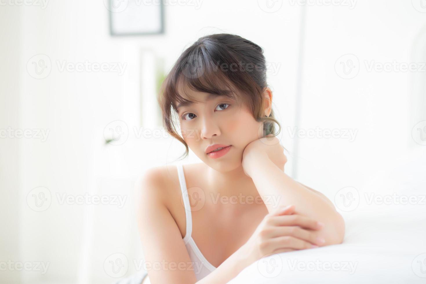 ritratto bella giovane donna asiatica sorriso mentre sveglia sano e benessere al mattino sul letto, bellezza asia ragazza felice sdraiato cura della pelle e trucco cosmetici in camera da letto, stile di vita e relax concetto. foto