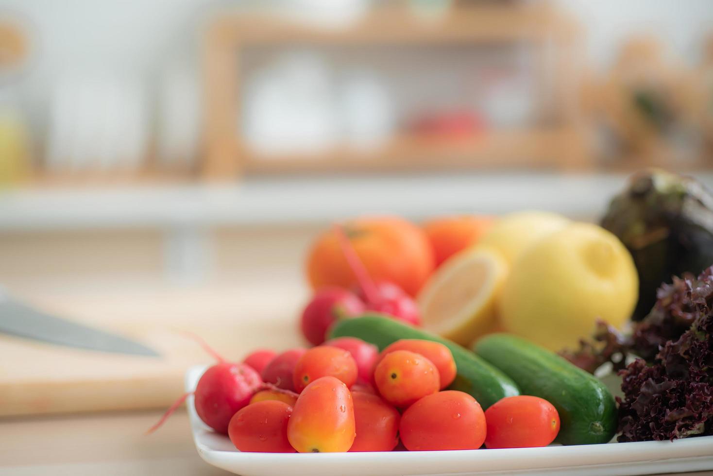 pomodorini vengono posti in un vassoio con ravanelli, cetrioli, lattuga di quercia rossa e altra frutta e verdura. come materia prima per fare le insalate sulla tavola della cucina. foto