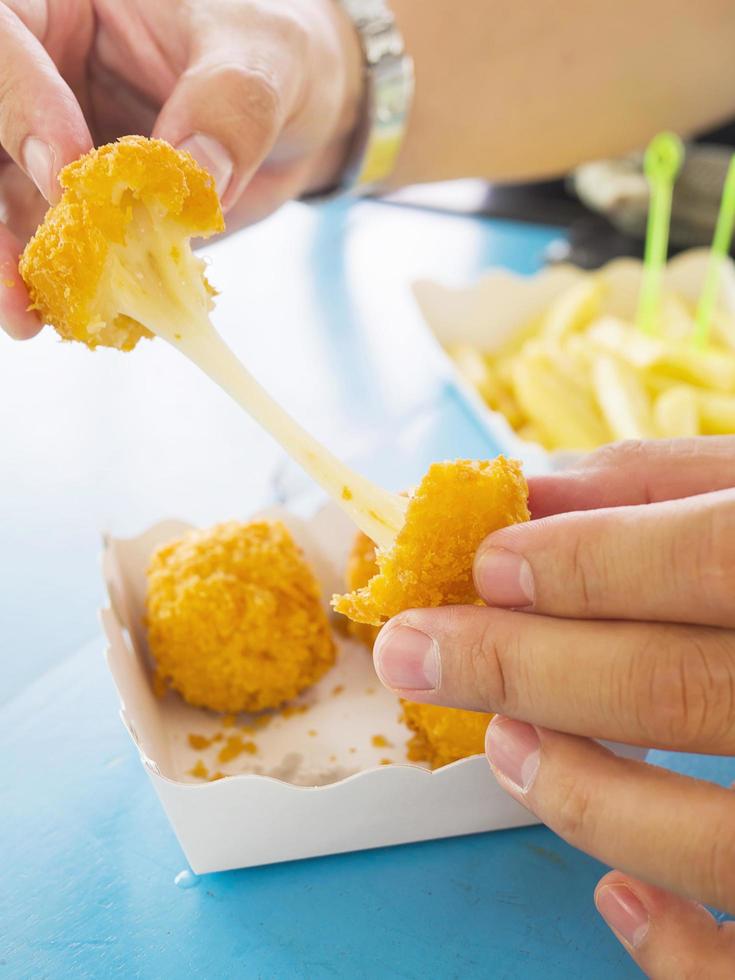 la mano tiene una palla di formaggio elastico pronta per essere mangiata con patatine fritte morbide focalizzate su sfondo blu del tavolo foto