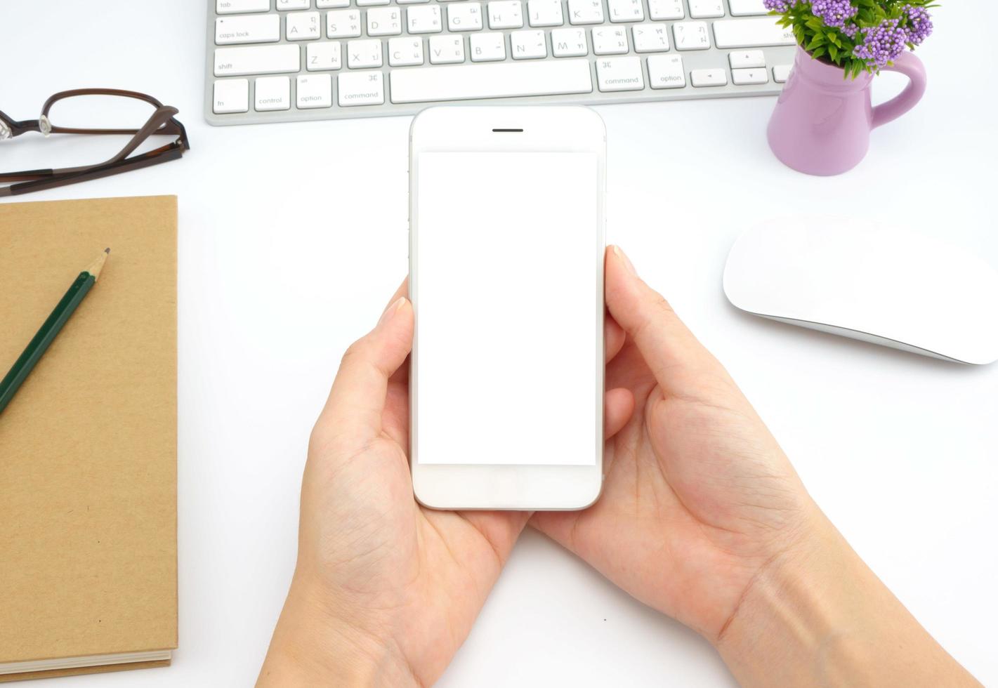 le mani della donna che tengono lo schermo vuoto dello smartphone sul lavoro di scrivania bianco. foto