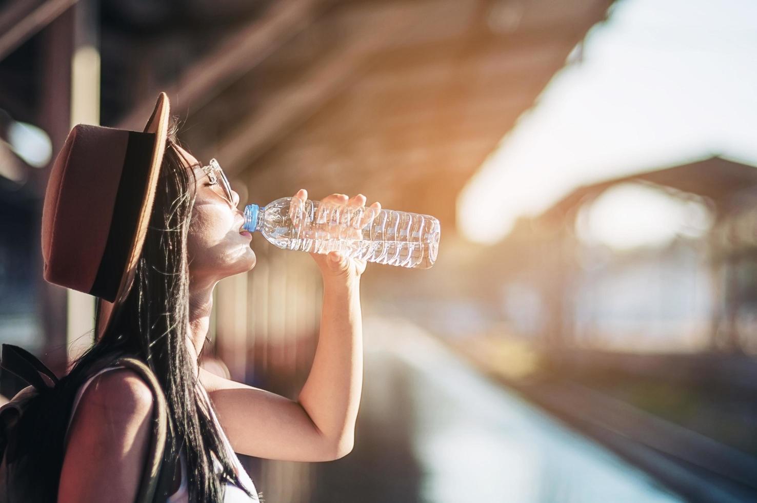il viaggiatore dello zaino della giovane donna beve acqua fresca nella stazione ferroviaria - concetto di attività del viaggiatore asiatico all'aperto foto