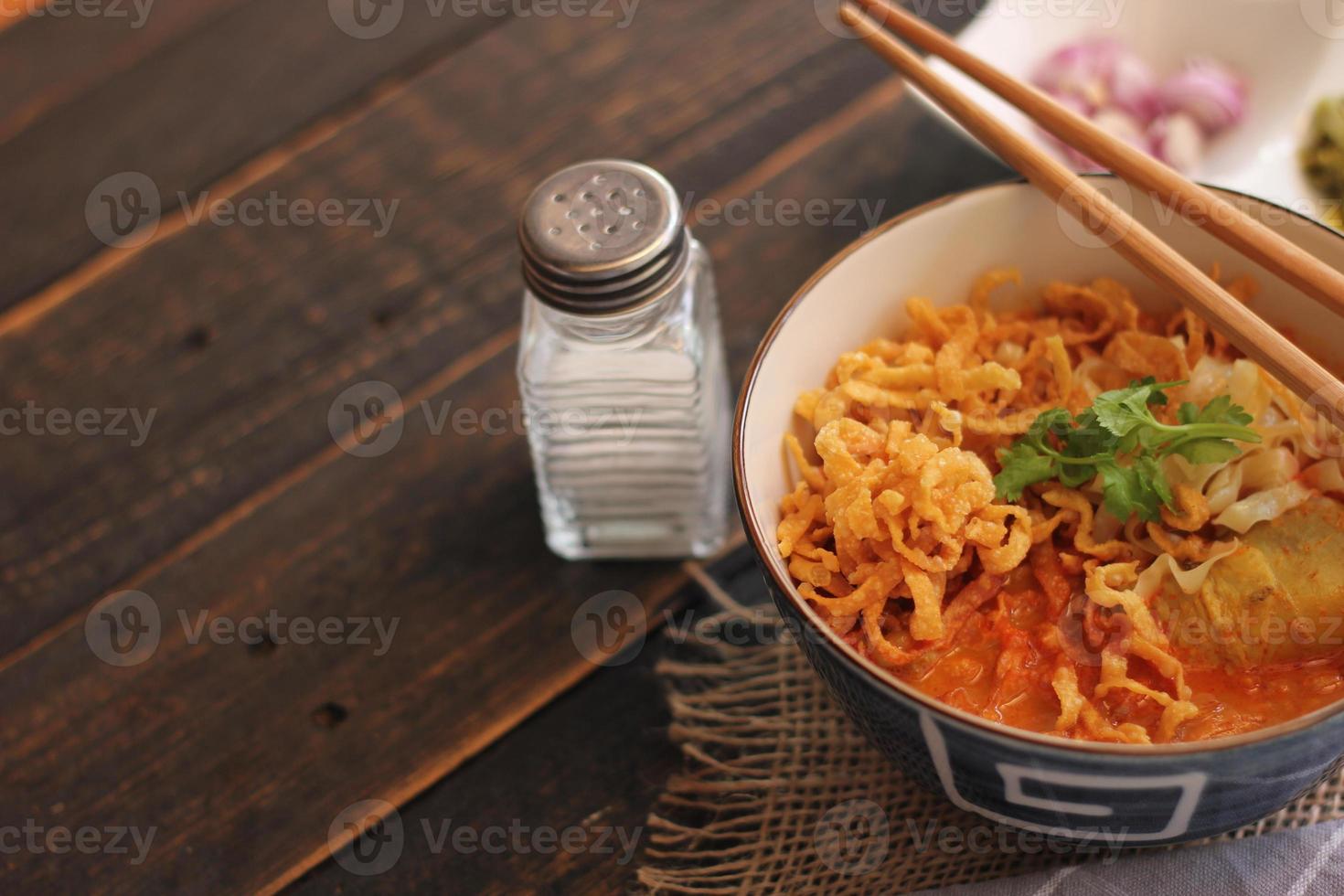 cibo tailandese, zuppa di noodle al curry in stile nordico servita in una ciotola con motivi in stile artistico. sul tavolo di legno nero foto