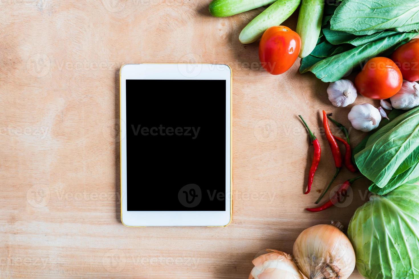 vista dall'alto di verdure fresche con gadget per computer touch tablet su sfondo tavolo in legno. foto