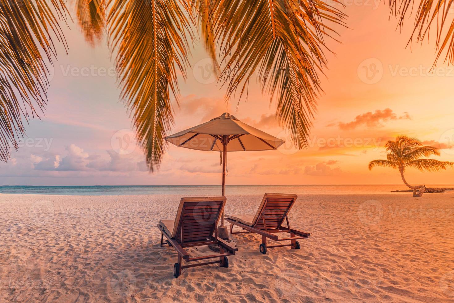 bellissimo scenario del tramonto tropicale, due lettini, lettini, ombrellone sotto la palma. sabbia bianca, vista mare con orizzonte, cielo crepuscolare colorato, calma e relax. hotel ispiratore del resort sulla spiaggia foto