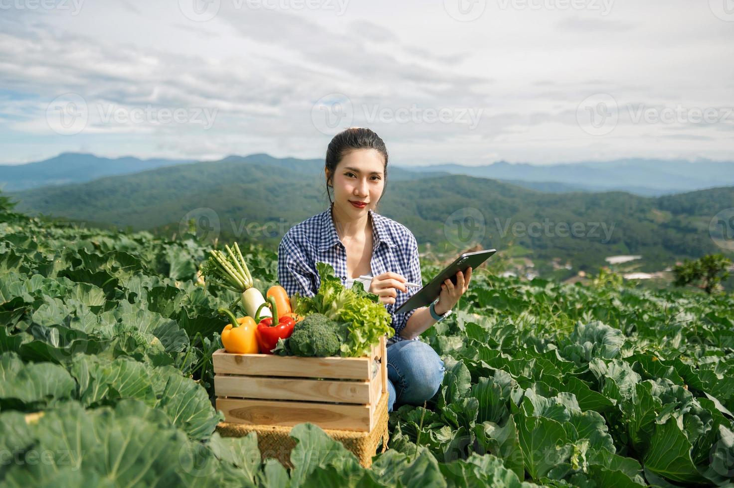 contadina asiatica che lavora presto nella fattoria che tiene cesto di legno di verdure fresche e tablet foto