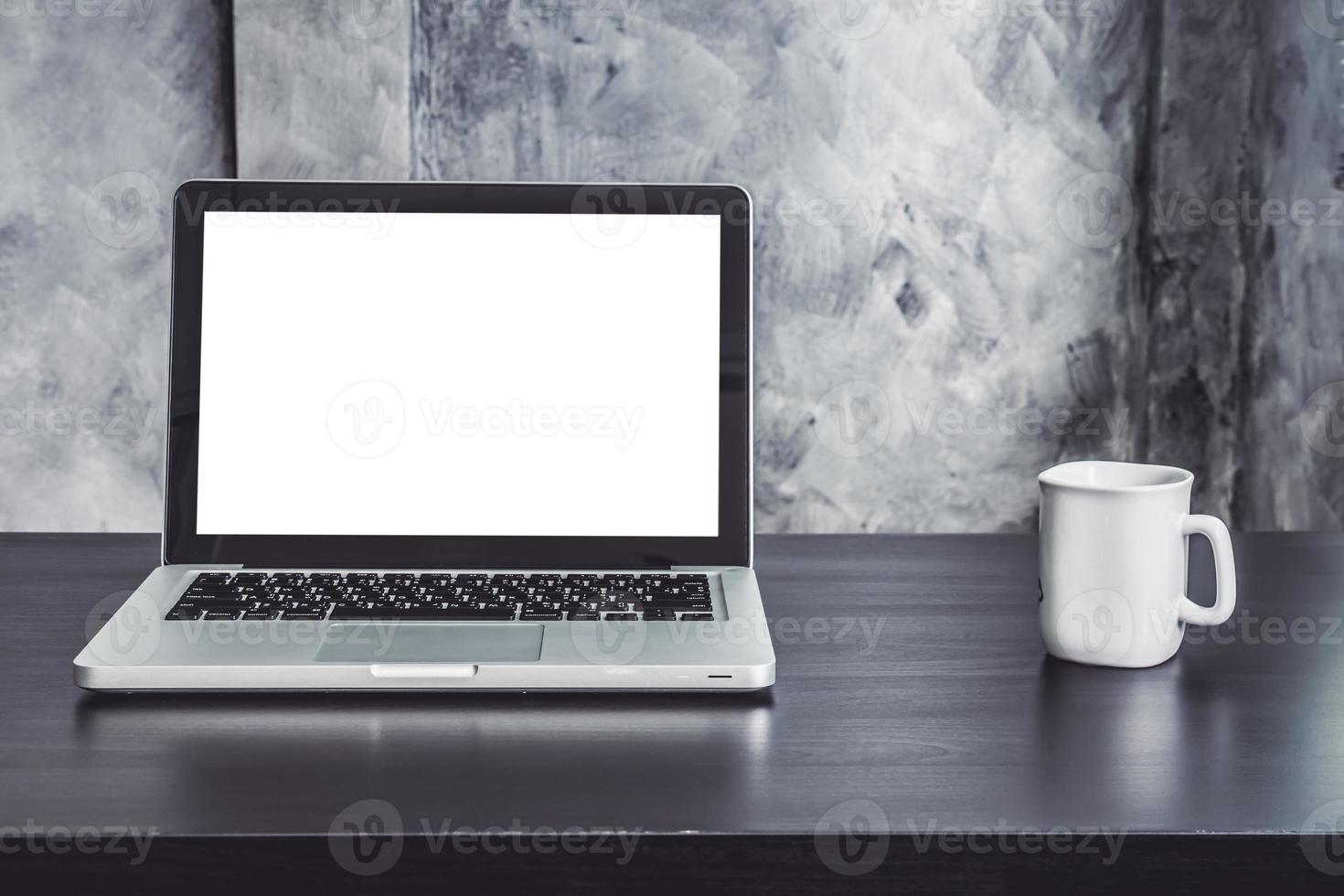 portatile con schermo bianco bianco e tazza di caffè bianca sulla scrivania foto