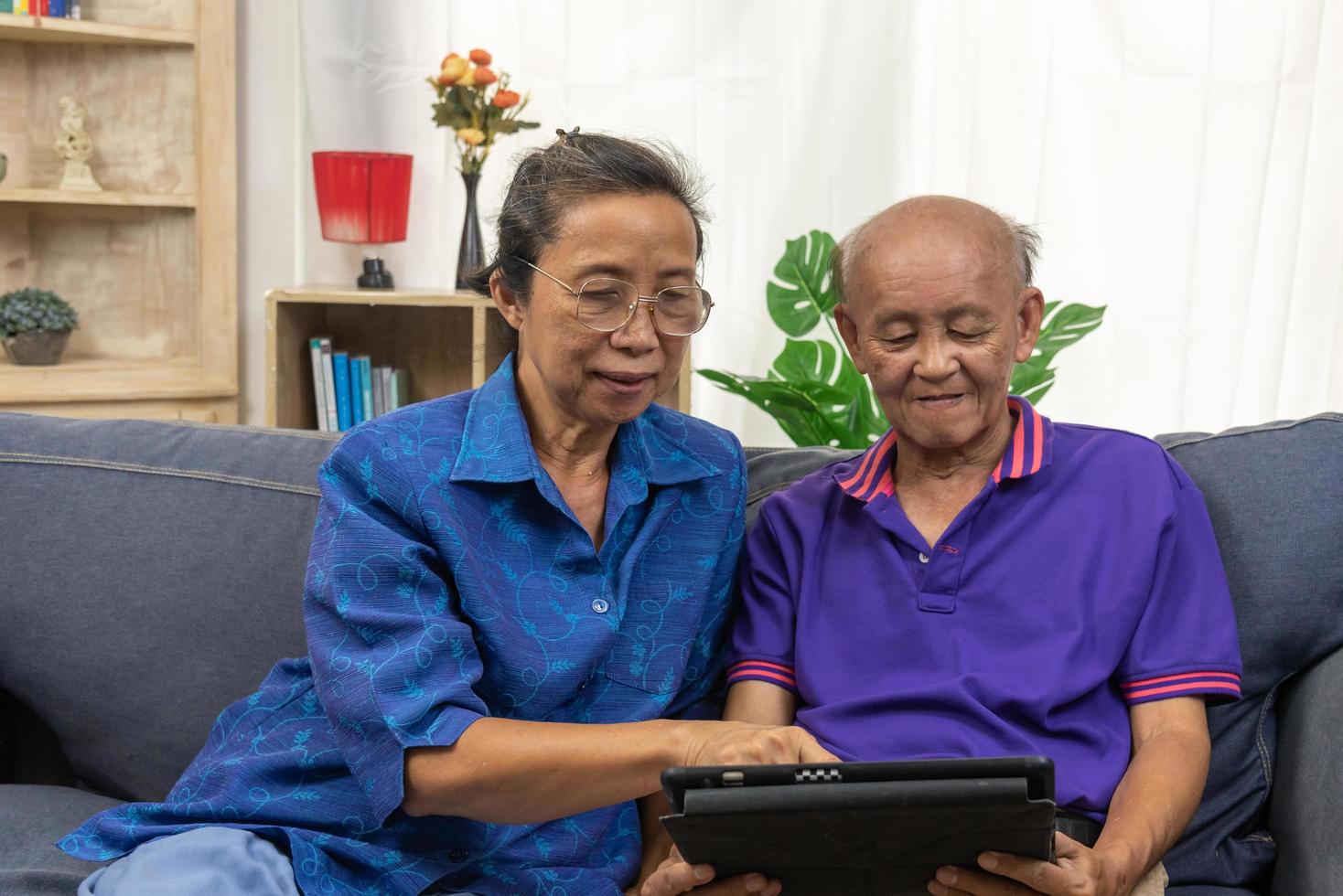 anziano asiatico che utilizza la tecnologia di comunicazione Internet online tablet sul divano di casa. foto