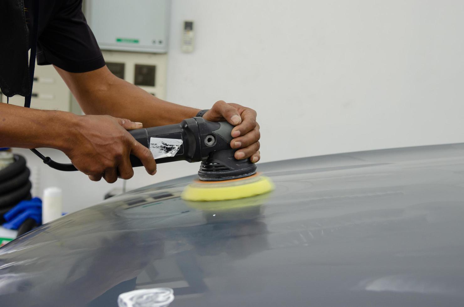 uomo che tiene lo strumento polacco meccanico di riparazione auto che dettaglia la manutenzione dei graffi dell'auto del cofano nel lavoro di autolavaggio del garage. foto