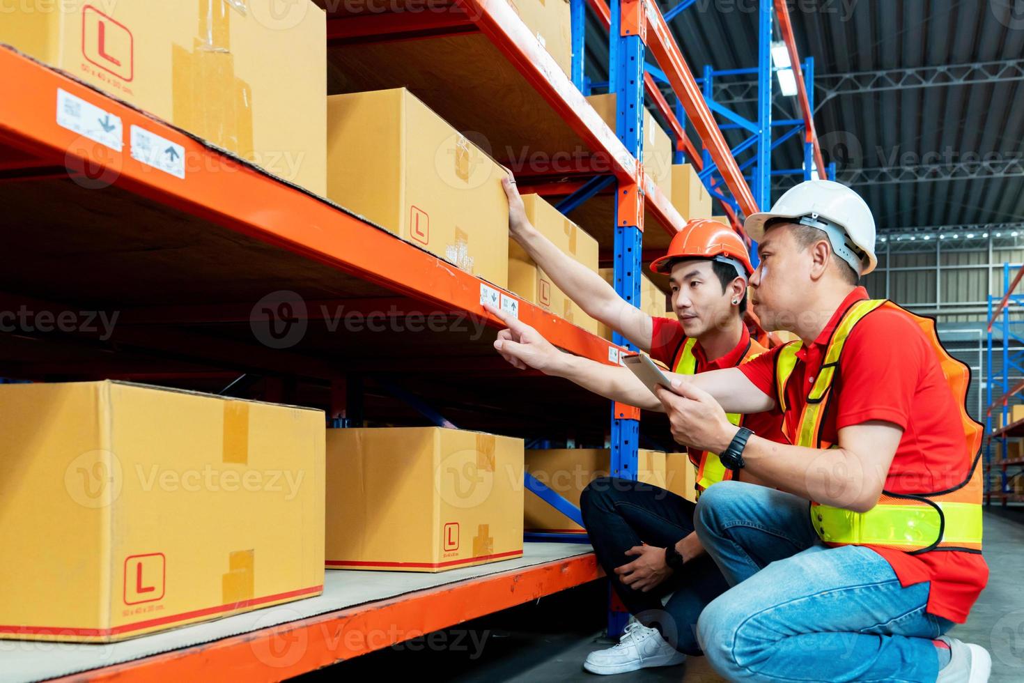 lavoratore maschio asiatico che parla con il manager nel magazzino. gli ingegneri dell'uomo le persone indossano un casco rigido di sicurezza e un giubbotto che controllano il pacco della scatola di immagazzinaggio in fabbrica. Bangkok, Tailandia foto