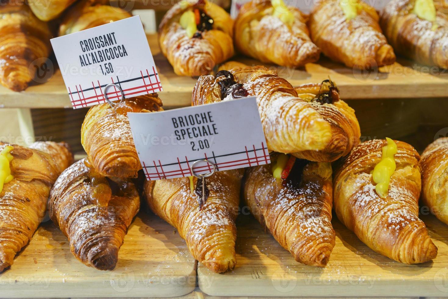 vari gusti di croissant o come in italia la loro chiamata brioche in mostra in una panetteria a milano, italia con un prezzo e un segno - albicocca significa marmellata in italiano foto