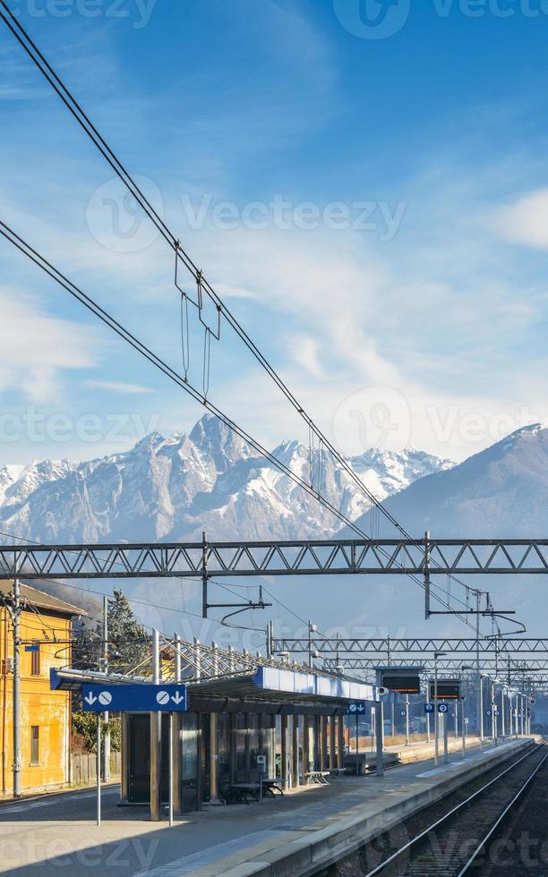 vista dal finestrino esterno del treno presso la piccola stazione ferroviaria e le maestose alpi italiane foto
