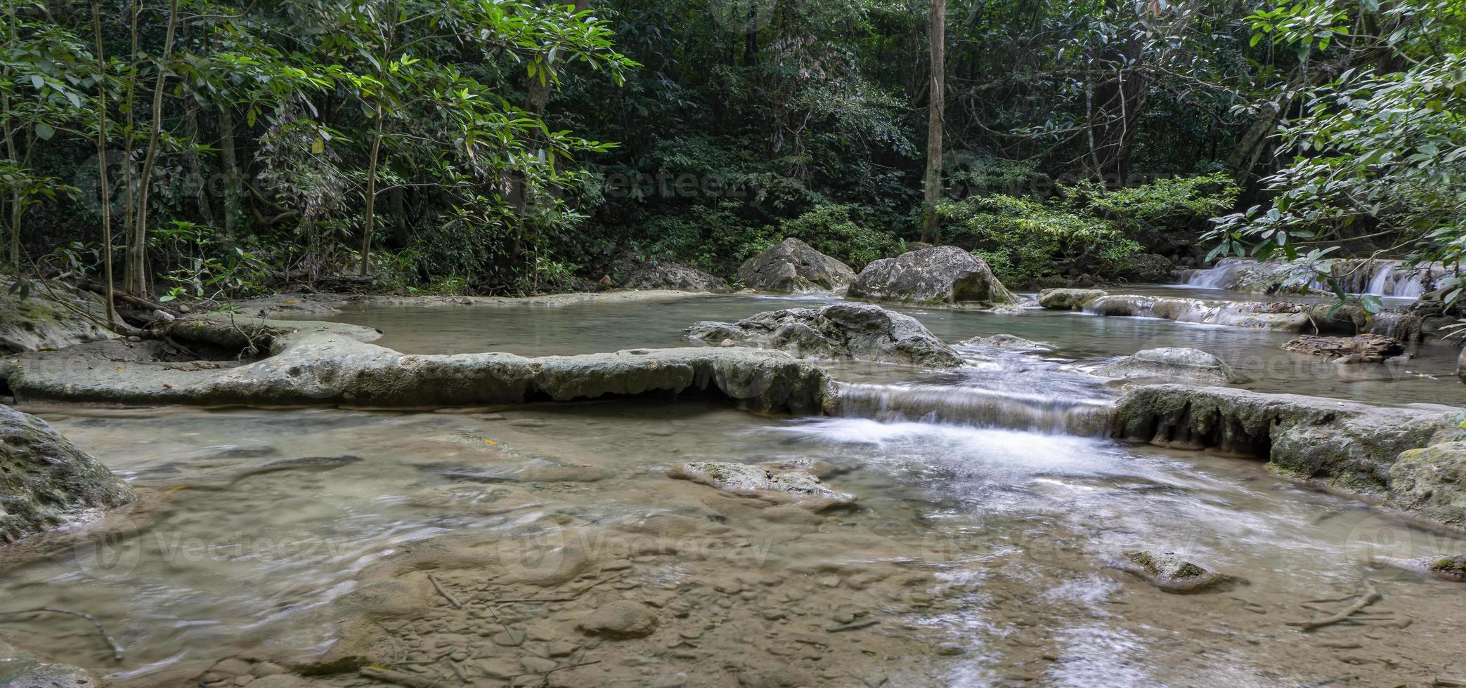 acqua verde smeraldo pulita dalla cascata circondata da piccoli alberi - grandi alberi, colore verde, cascata di erawan, provincia di kanchanaburi, tailandia foto