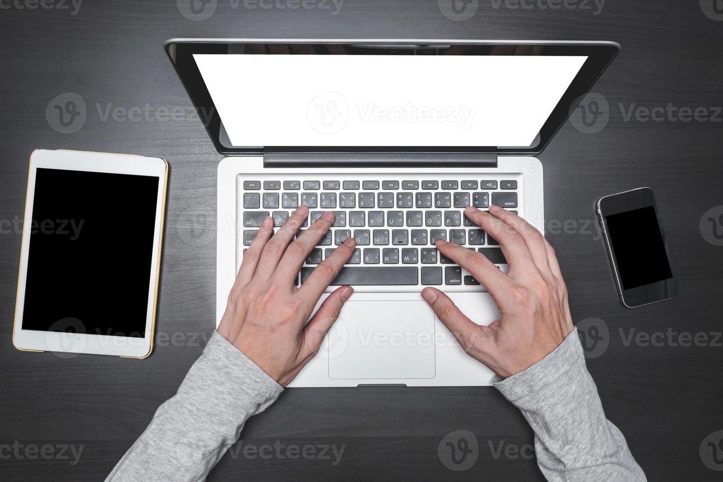 vista dall'alto delle mani maschili che lavorano su laptop con tablet e smartphone su sfondo nero scrivania in legno. foto