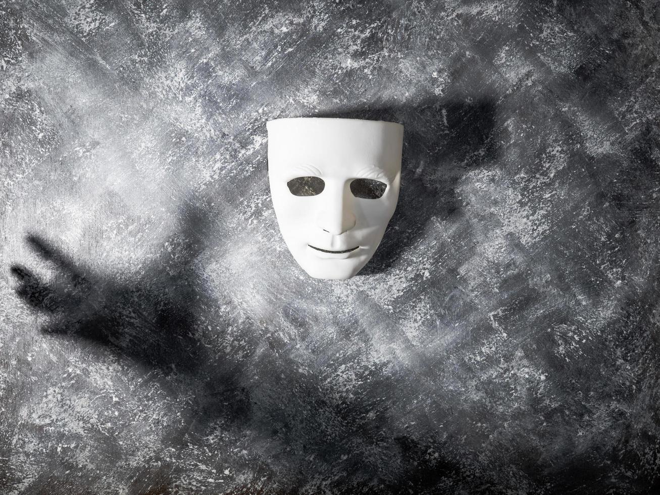 maschera bianca con ombra della mano su sfondo grigio grunge. foto