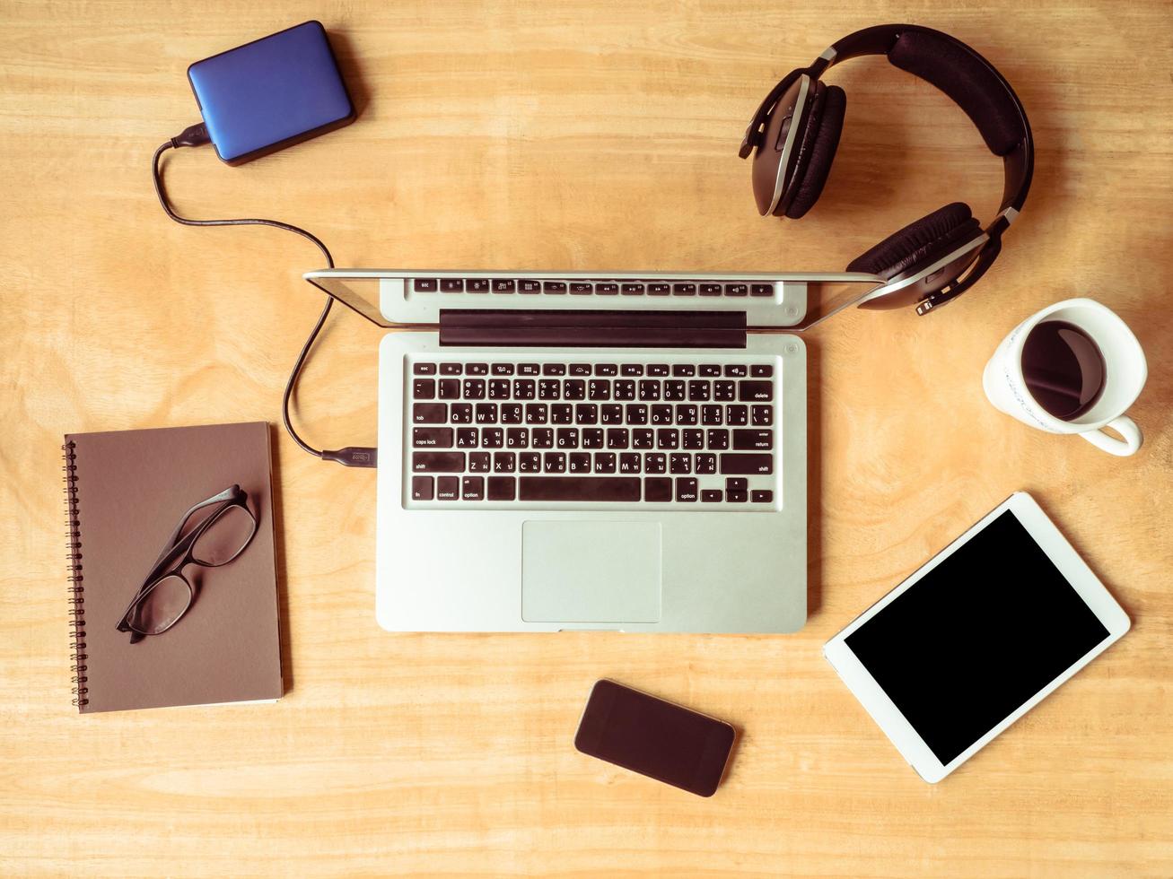 vista dall'alto di dispositivi elettronici con notebook, occhiali e tazza di caffè su sfondo tavolo in legno. foto