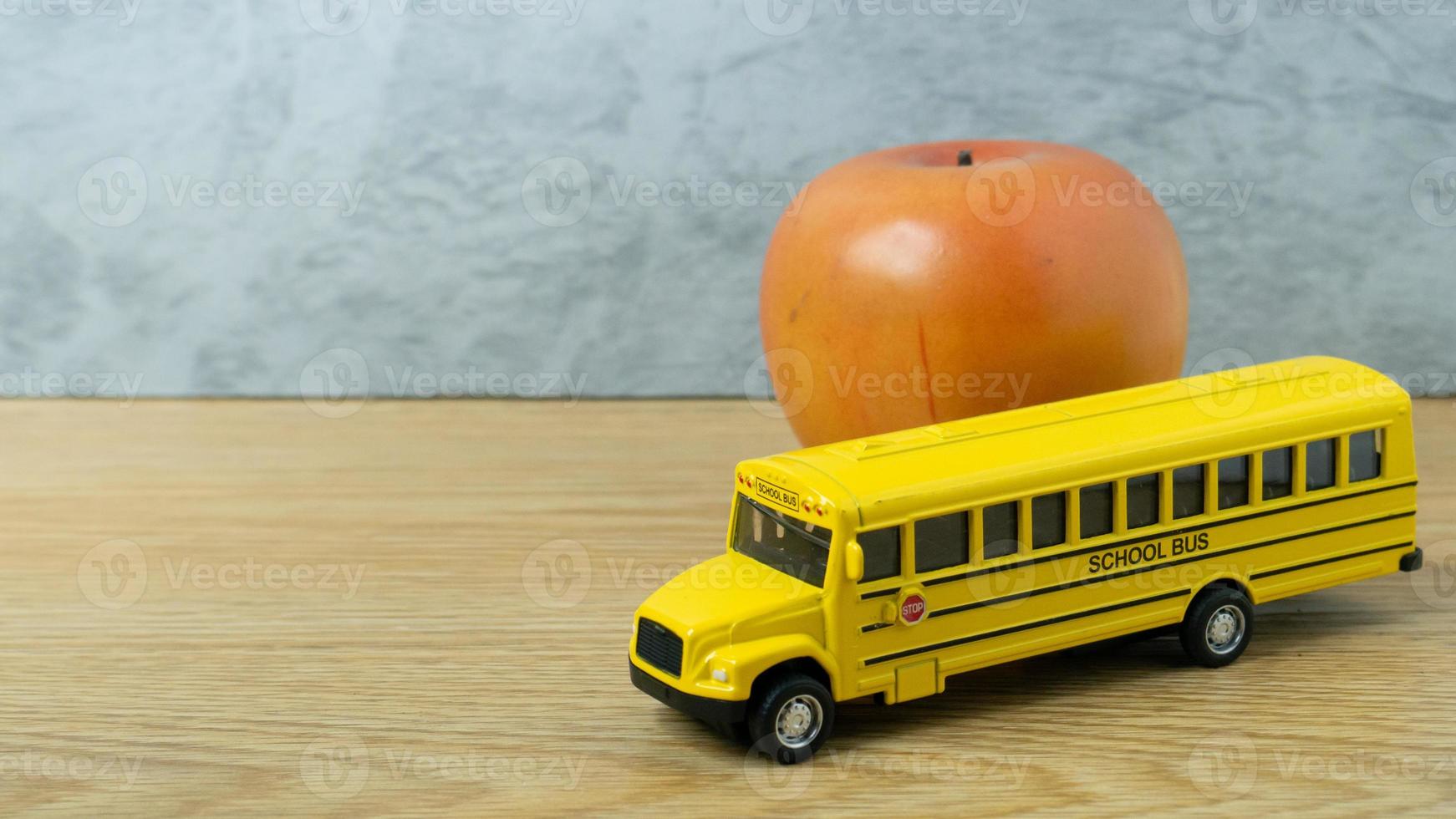 il giocattolo dello scuolabus e la mela sul tavolo di legno per il ritorno a scuola o il concetto di istruzione foto