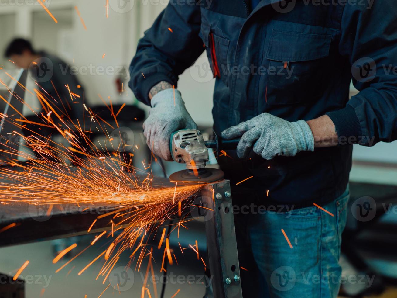 interno di una fabbrica di ingegneria dell'industria pesante con un lavoratore industriale che utilizza una smerigliatrice angolare e taglia un tubo di metallo. appaltatore in uniforme di sicurezza e elmetto per la produzione di strutture metalliche. foto