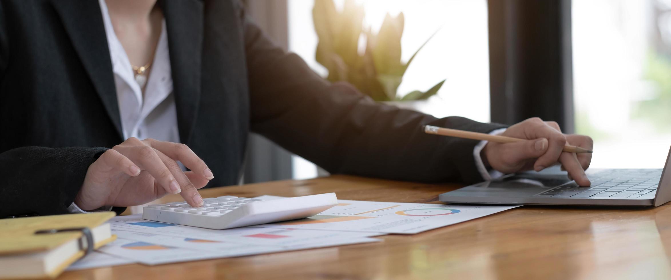 primo piano della mano della donna d'affari utilizzando una calcolatrice e prendere appunti per controllare le finanze dell'azienda, i guadagni e il budget. foto