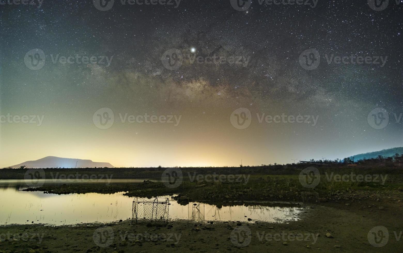 le stelle nel cielo riflettono la luce di notte. la via lattea sopra le montagne e lo stagno diga e bacino idrico di mae prachan, phetchaburi, thailandia foto