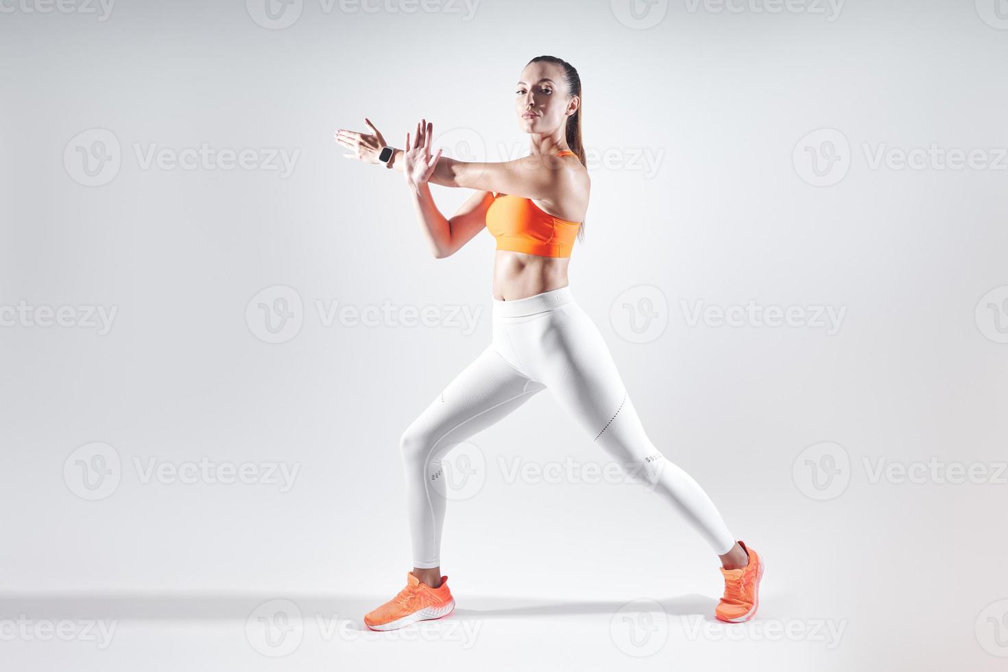 giovane donna sicura di sé in abbigliamento sportivo facendo esercizi di stretching su sfondo bianco foto