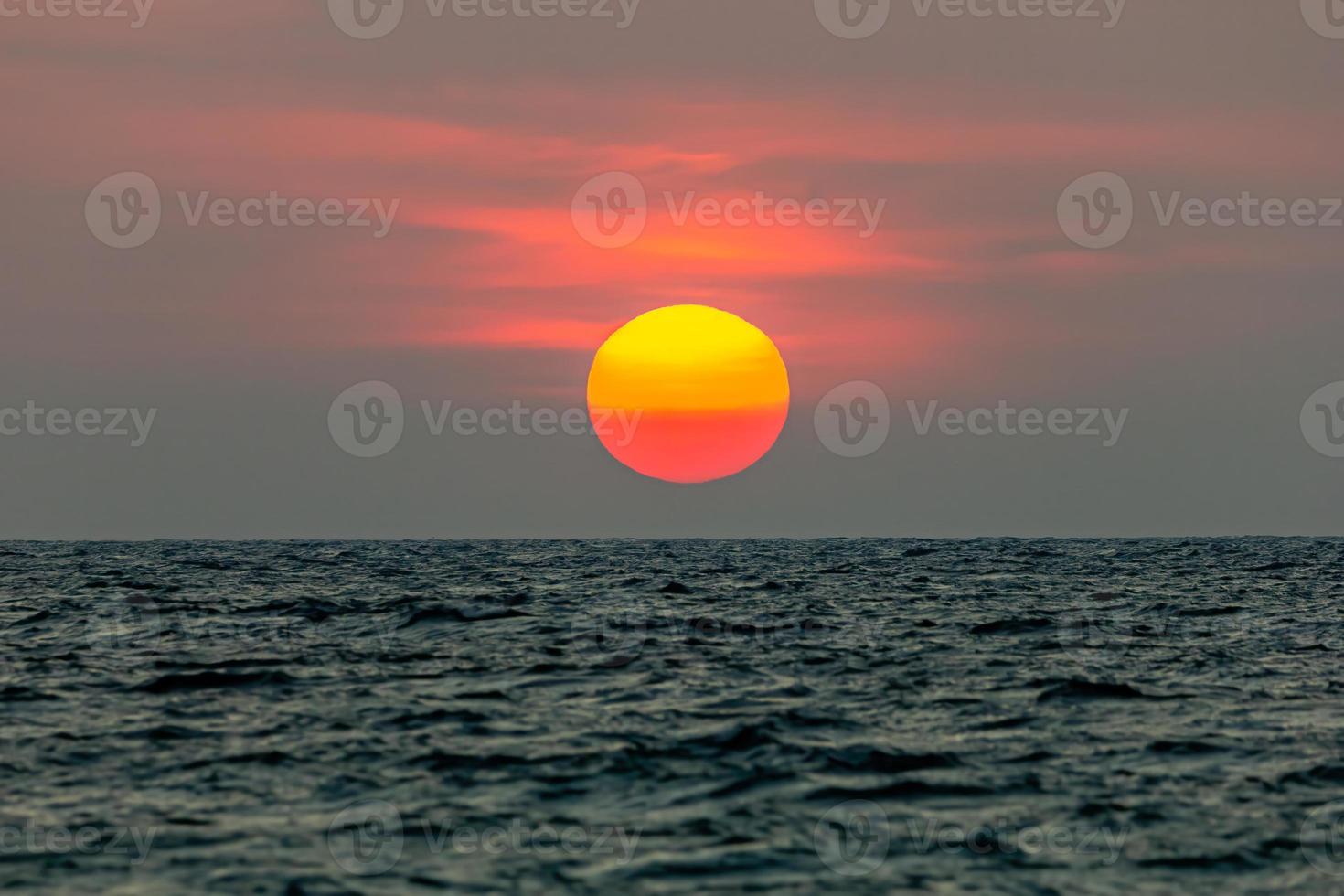 il sole sta cadendo nel mare. , il cielo è arancione e il mare è scuro foto