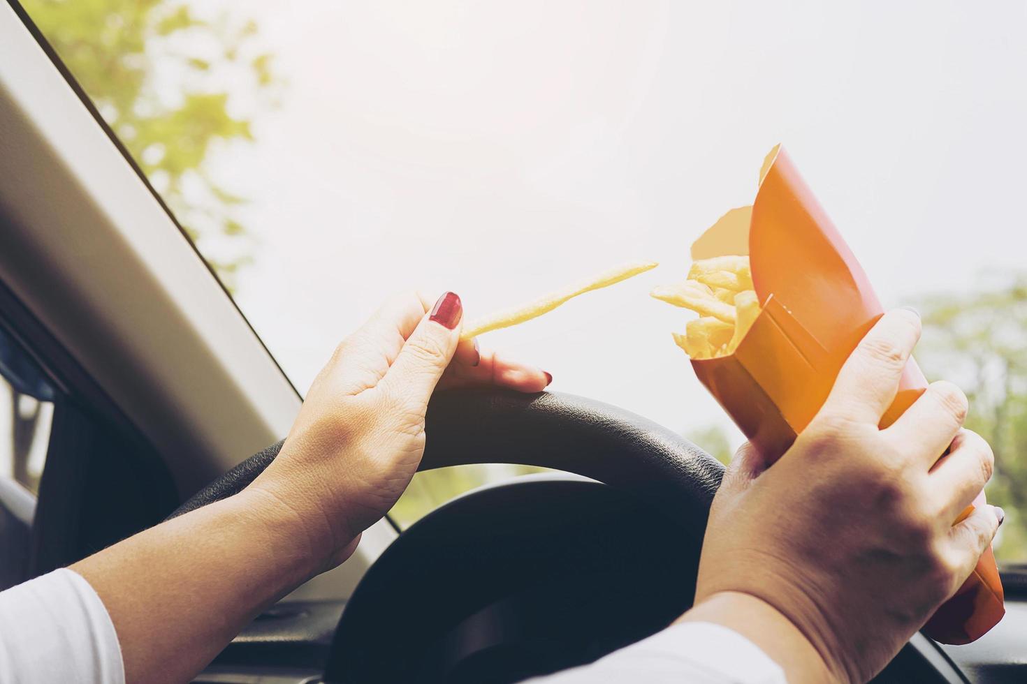 signora che mangia le patatine fritte bianche che guida l'auto pericolosamente foto