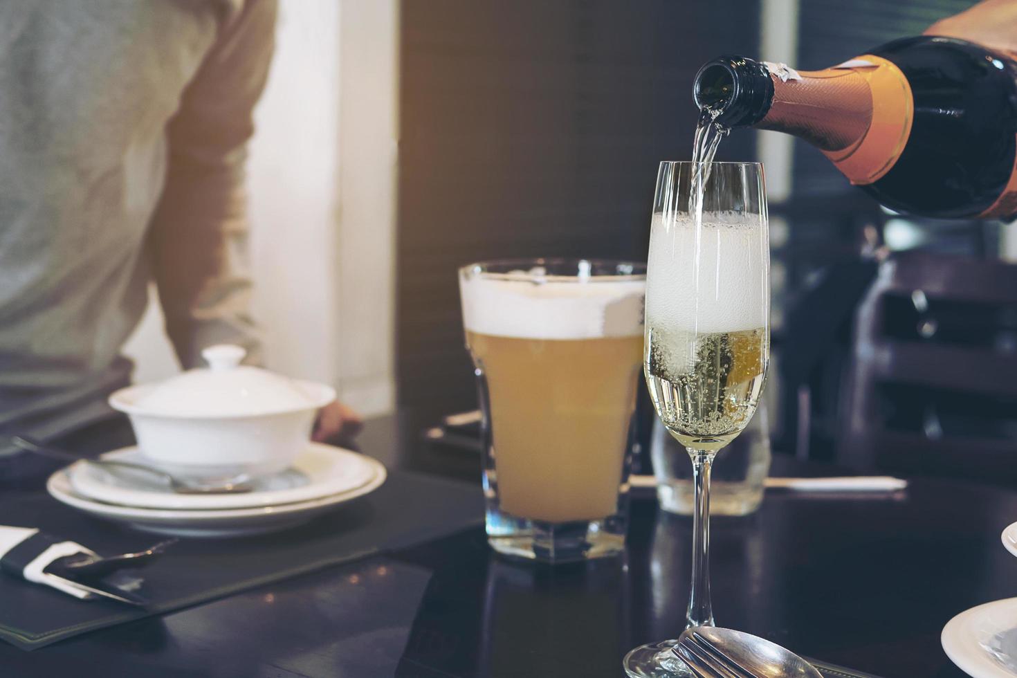 mano dell'uomo che versa champagne in un bicchiere pronto da bere sul tavolo sfocato nel ristorante - persone in festa felice celebrazione e concetto di servizio aziendale ristorante foto