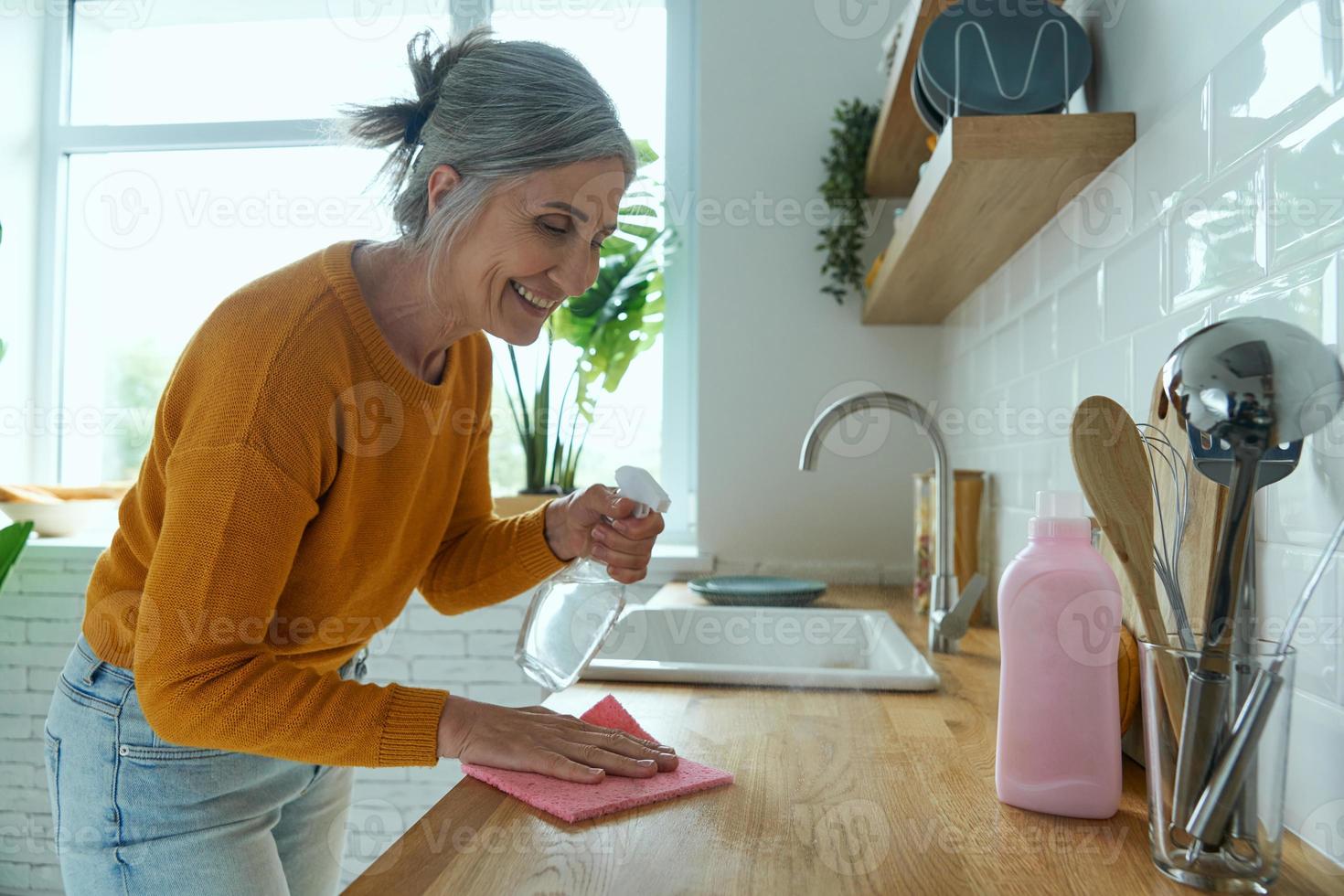 donna anziana fiduciosa che riordina il bancone della cucina e sorride foto