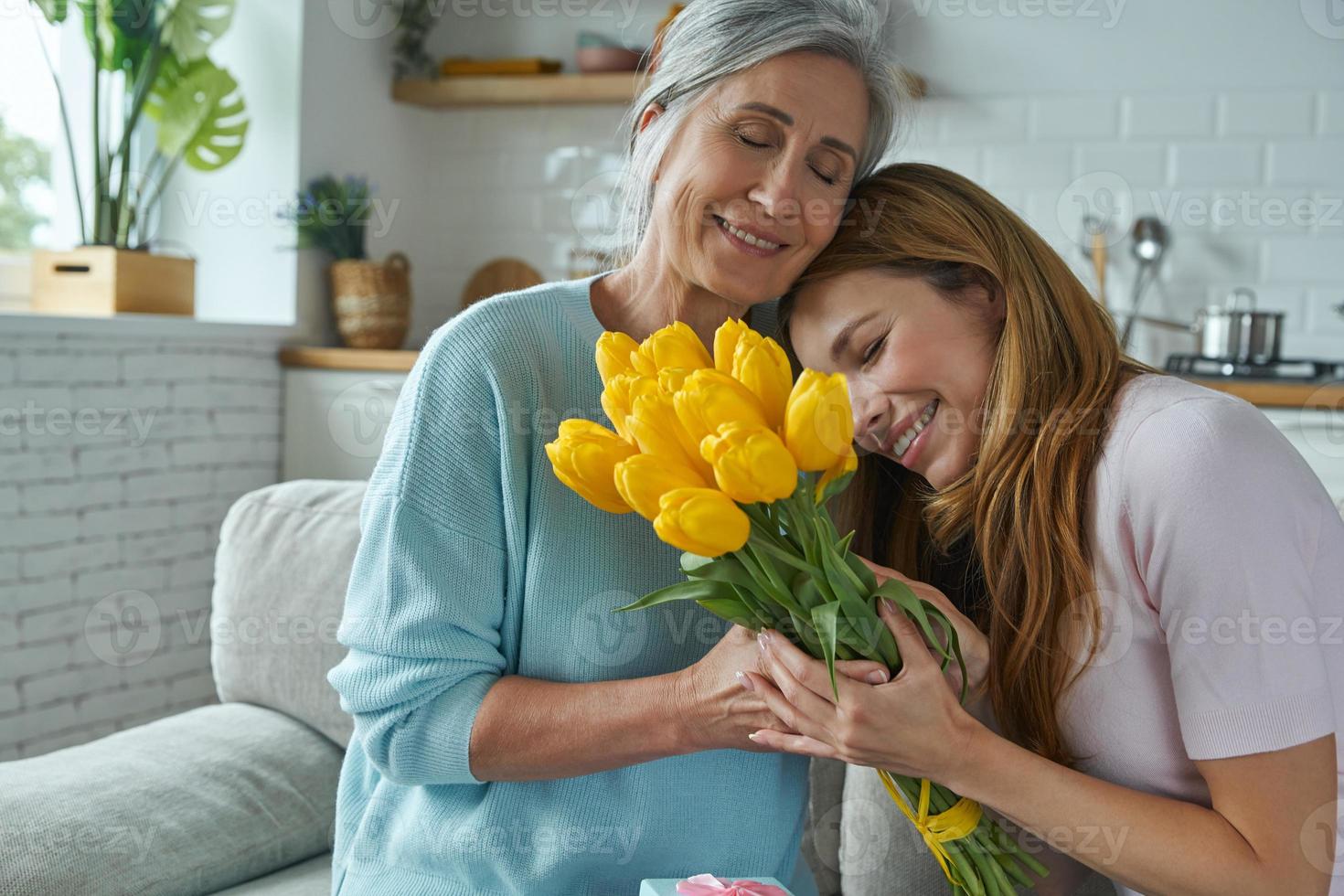 gioiosa madre senior che riceve una confezione regalo e un mazzo di tulipani da sua figlia foto