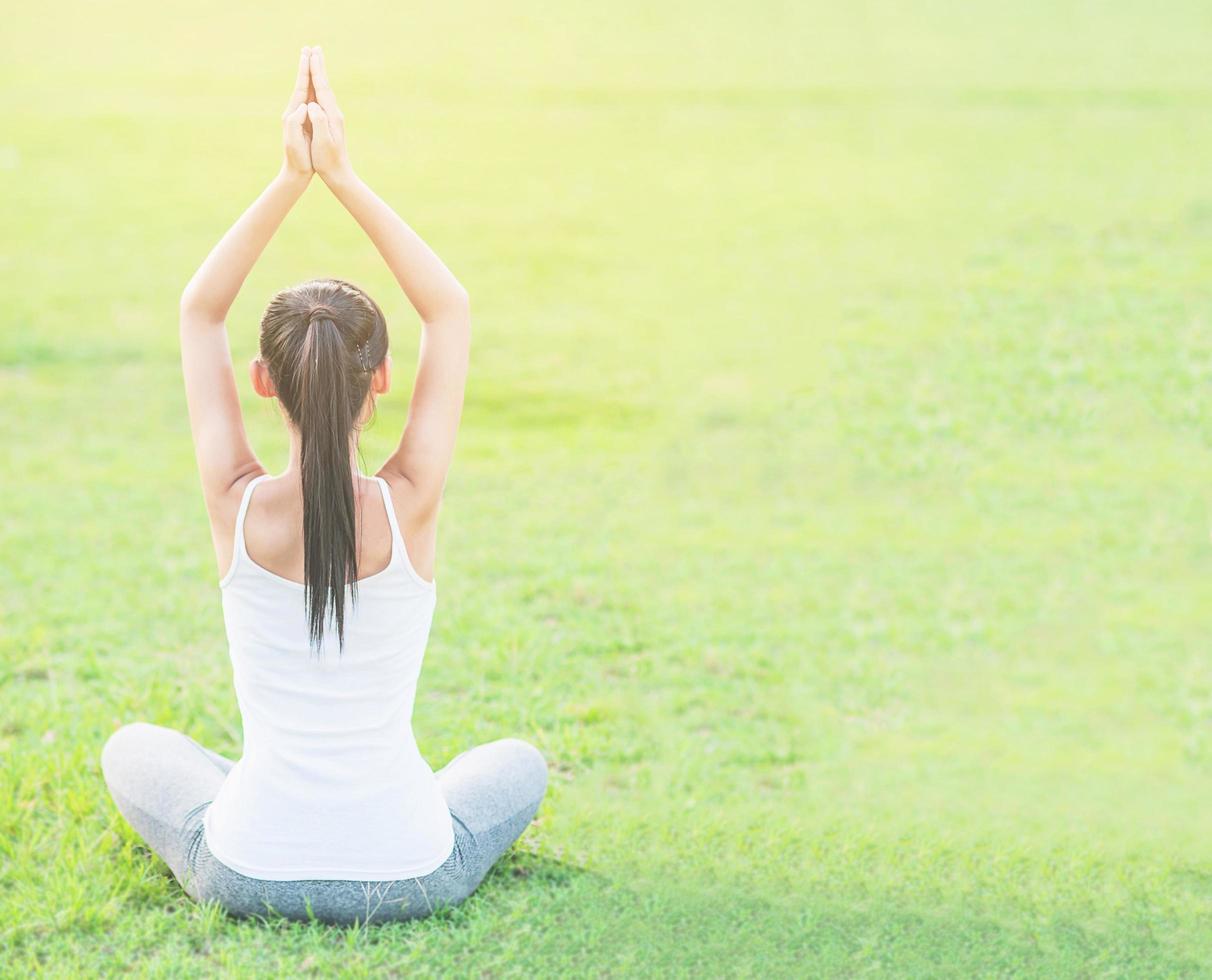 giovane donna che fa esercizio di yoga nell'area all'aperto del campo verde che mostra la calma pacifica nella mente di meditazione - le persone praticano lo yoga per la meditazione e il concetto di esercizio foto