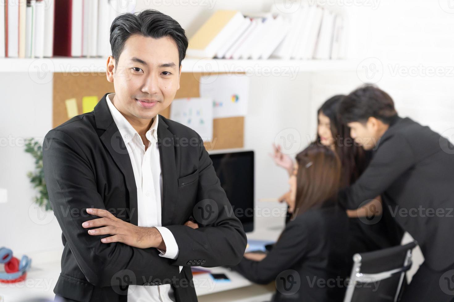 uomo d'affari sorridente felice in piedi con le braccia incrociate gesto in ufficio durante la riunione di lavoro. foto