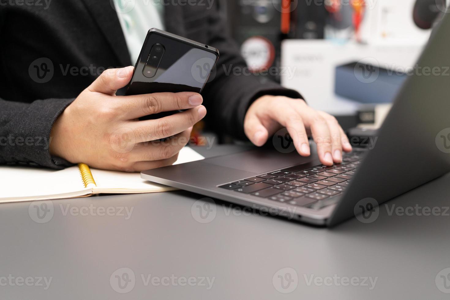 organizzare il processo di lavoro nel proprio blocco note gustando un gustoso cappuccino seduto al chiuso al computer portatile. lavorando sulla scrivania con laptop e smartphone. foto