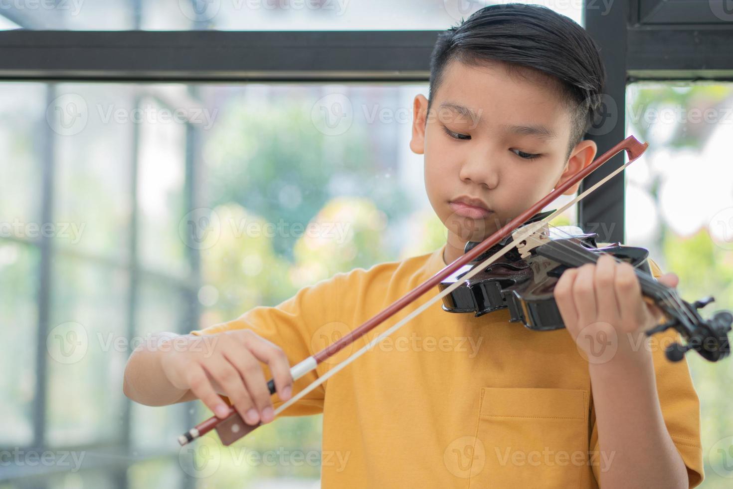 un ragazzino asiatico che suona e pratica lo strumento a corda musicale del violino contro in casa, concetto di educazione musicale, ispirazione, studente di scuola d'arte per adolescenti. foto