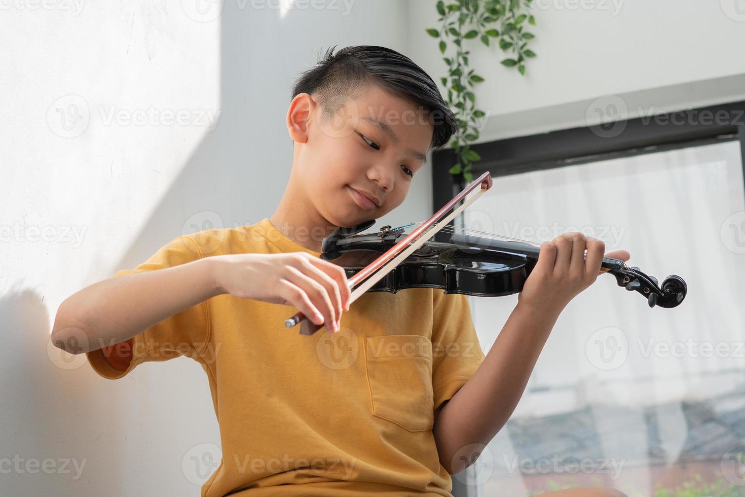 un ragazzino asiatico che suona e pratica lo strumento a corda musicale del violino contro in casa, concetto di educazione musicale, ispirazione, studente di scuola d'arte per adolescenti. foto