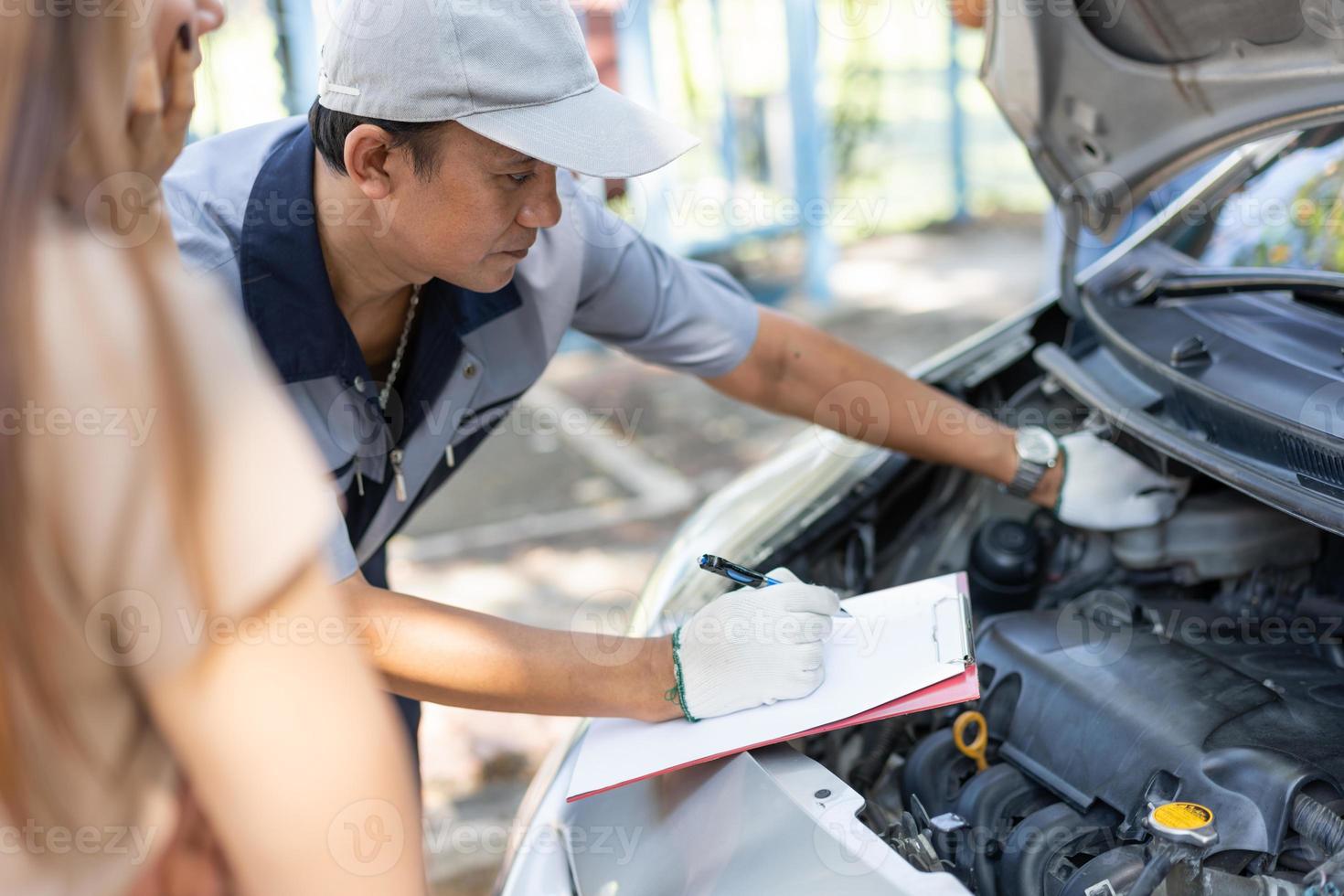 il meccanico asiatico maschio tiene un blocco per appunti ed esamina il problema di guasto del motore dell'auto con il cliente femminile e spiega la causa principale e stima il preventivo di riparazione, la riparazione dell'auto e il concetto di manutenzione. foto