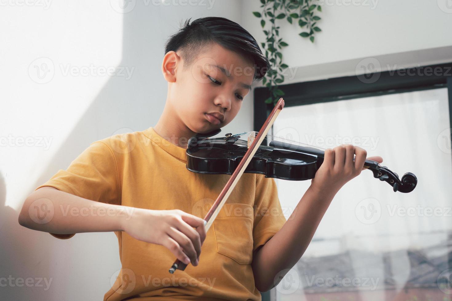 un ragazzino asiatico che suona e pratica lo strumento a corda musicale del violino contro in casa, concetto di educazione musicale, ispirazione, studente di scuola d'arte per adolescenti. foto