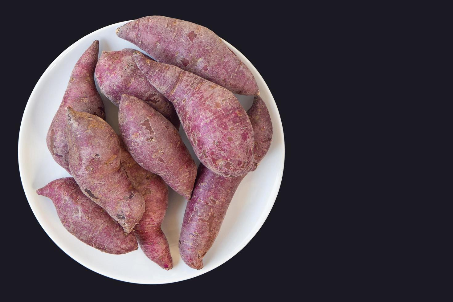 primo piano della pila di patate dolci viola fresca sul piatto bianco con sfondo nero foto