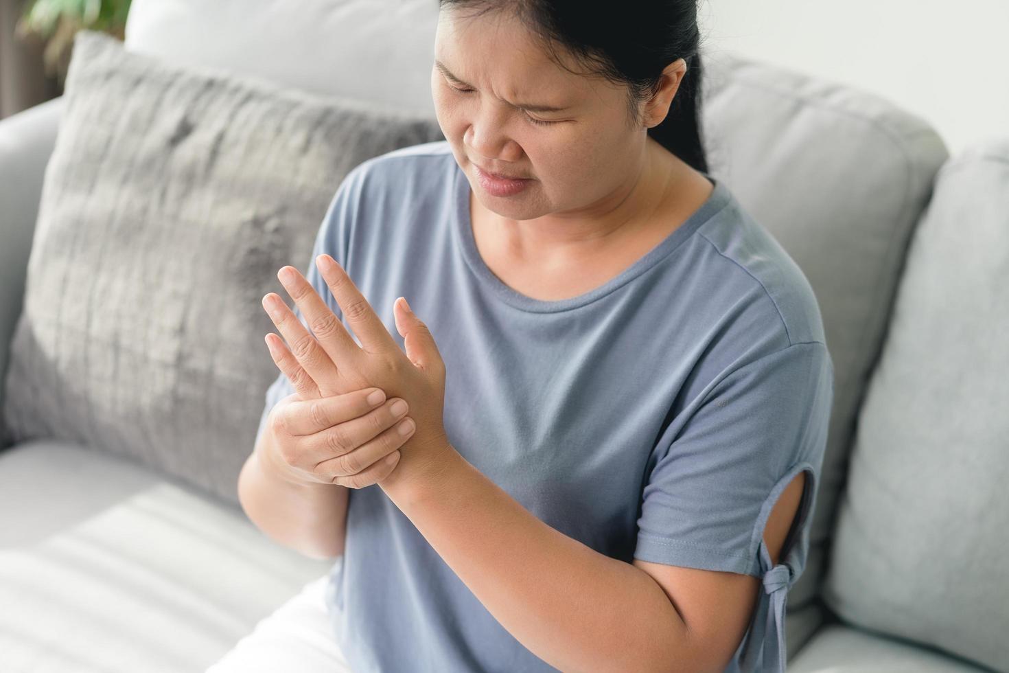 la donna del primo piano che si siede sul sofà le tiene il polso. ferita alla mano, sensazione di dolore. assistenza sanitaria e concetto medico. foto