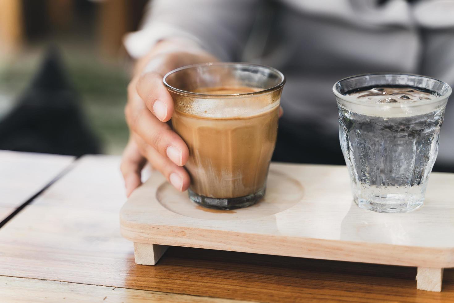 donna tiene in mano un bicchiere di caffè espresso girato sopra il latte fresco freddo. caffè sporco, menu del caffè, caffè al latte foto